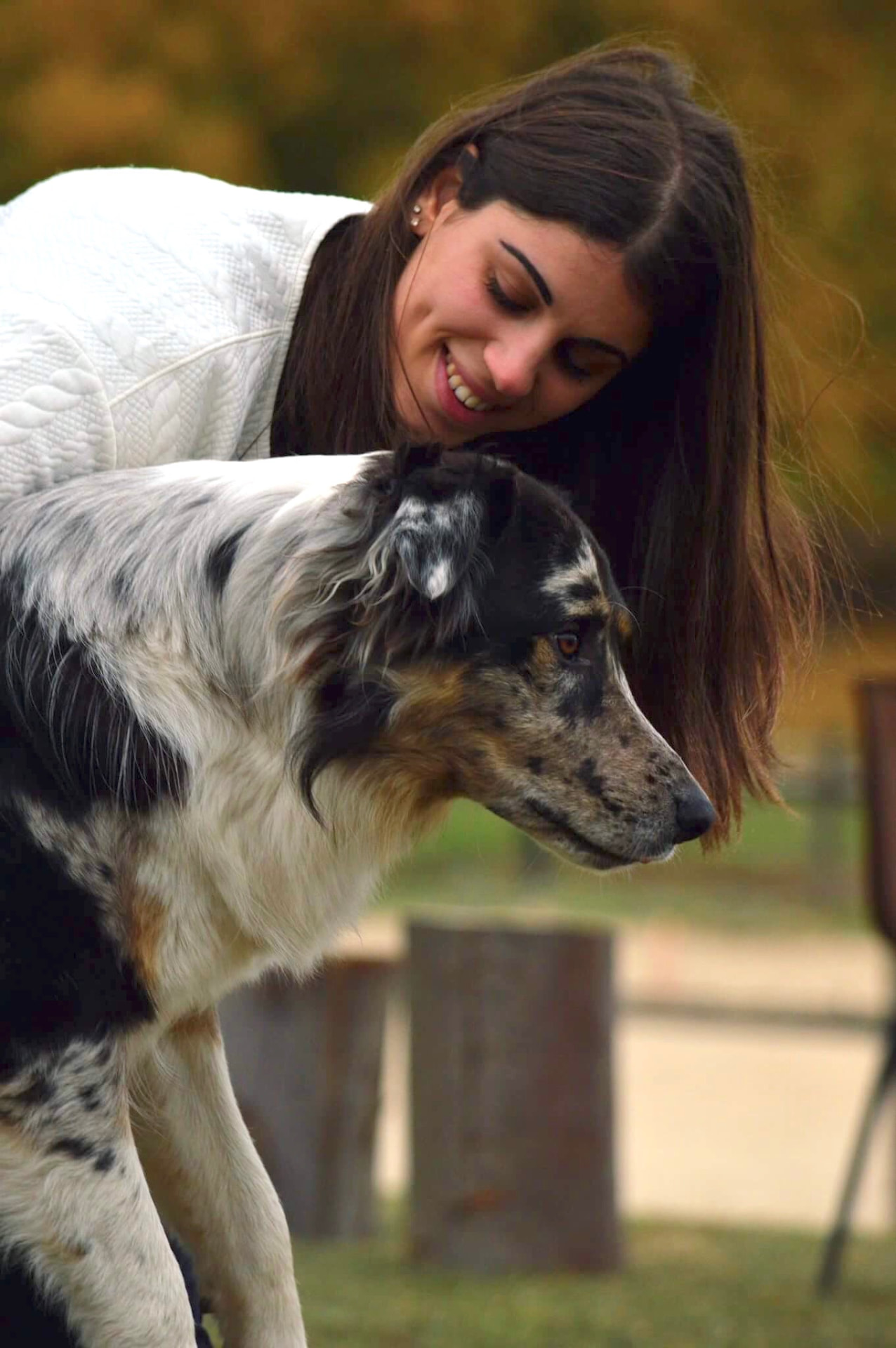 Lia, responsable du domaine, penchée avec un chien tacheté gris et noir, dans un moment de complicité